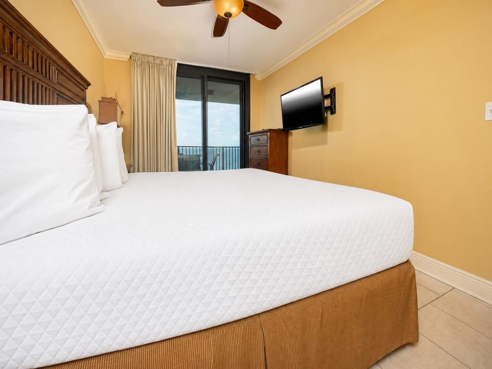 Cozy master bedroom featuring a plush king bed, flat-screen TV, and access to the beachfront balcony