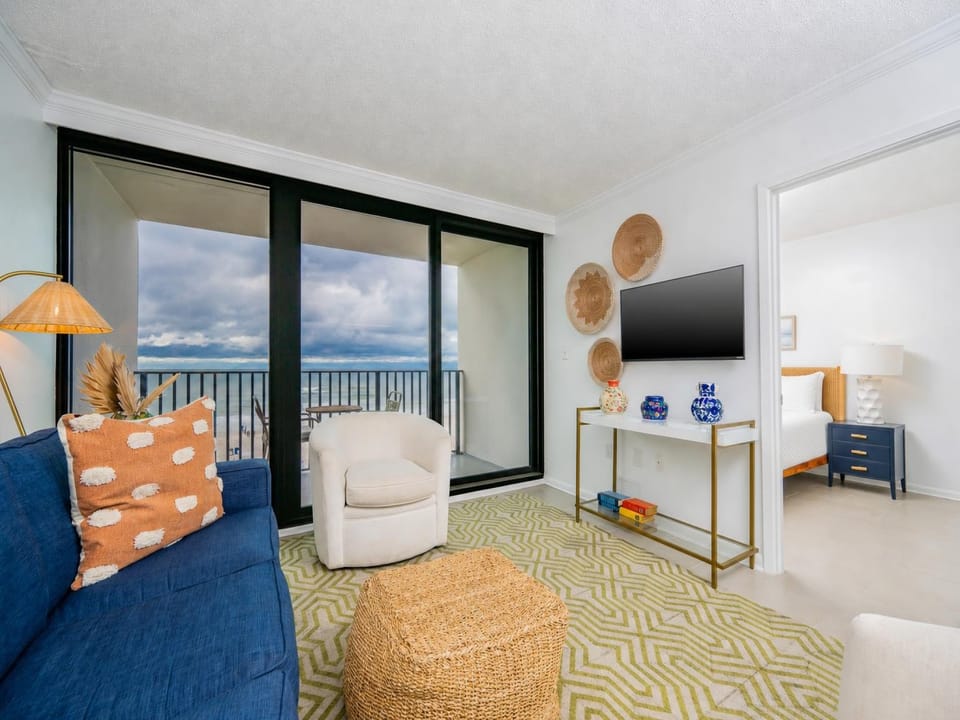 The inviting living area features a cozy blue sofa, a flat-screen TV, and stunning beachfront views through large glass doors