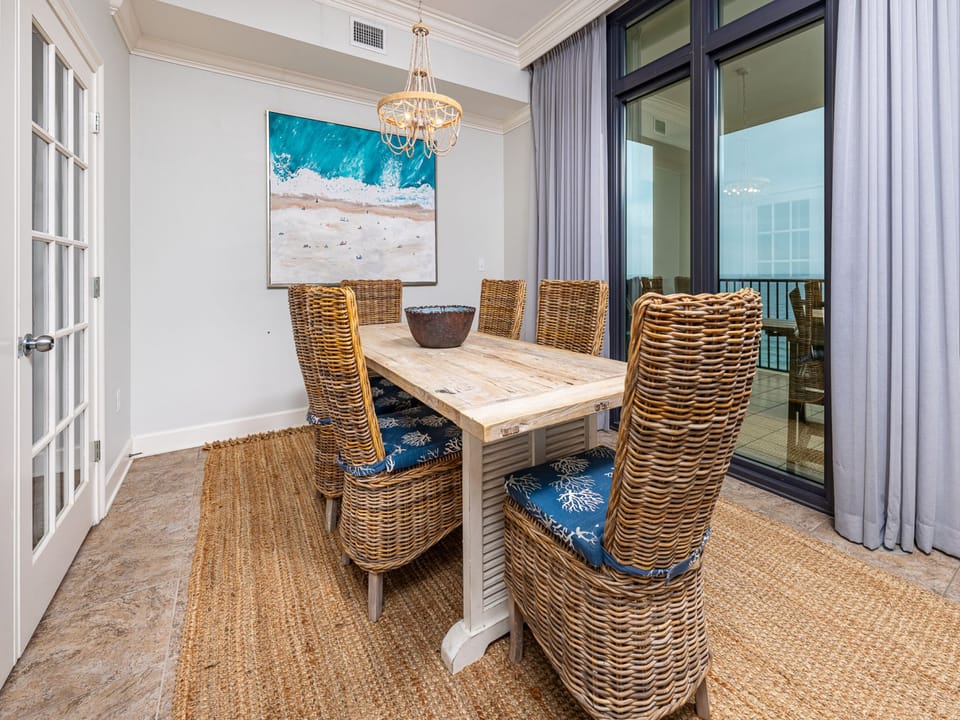 This dining area features a rustic table surrounded by woven chairs, with a stunning beachfront view through large windows