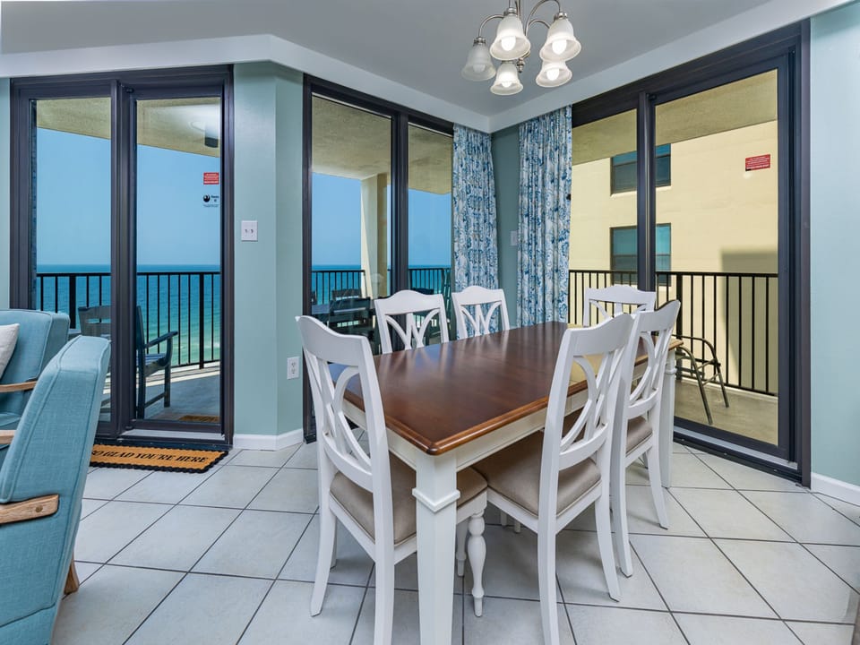 A stylish dining table with six chairs and large windows showcasing a beach front view