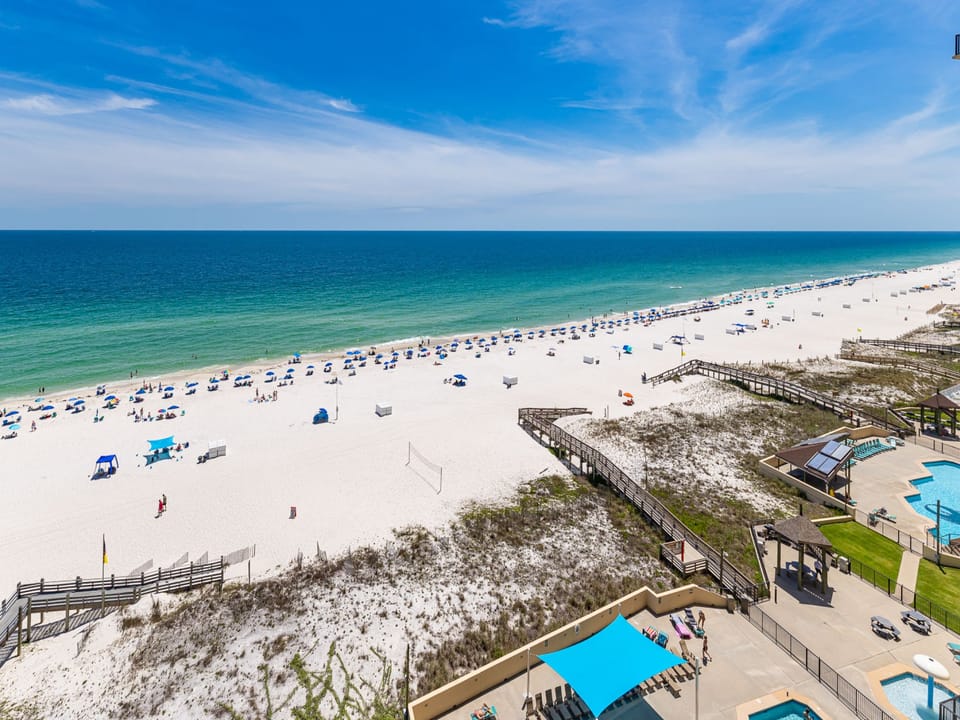 A panoramic view reveals vibrant blue umbrellas lining a pristine beach with soft white sand under a clear blue sky