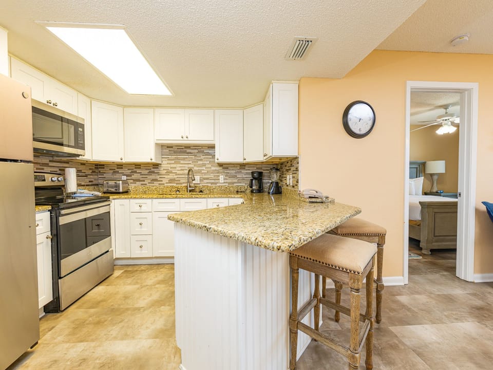 Kitchen features sleek cabinetry, a granite countertop breakfast bar with seating, and a view into the master suite