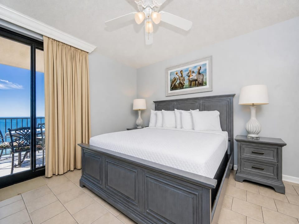 Unwind in this spacious master bedroom featuring a king bed, lamp, and a view of the balcony with beachfront views
