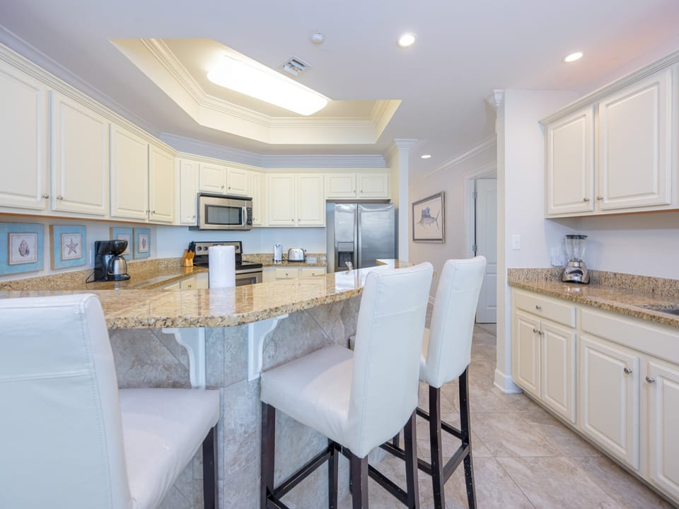 Kitchen featuring sleek stainless appliances and a spacious granite countertop with stylish white bar stools