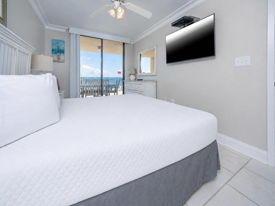 Comfortable master bedroom features a large king bed, a mounted TV, and sliding glass doors leading to the beachfront balcony