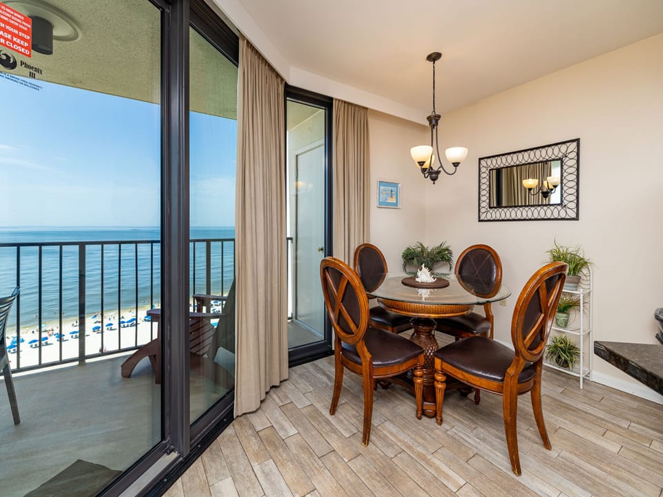 A glass-top dining table surrounded by dark wood chairs offers a view of the beach through expansive sliding glass doors