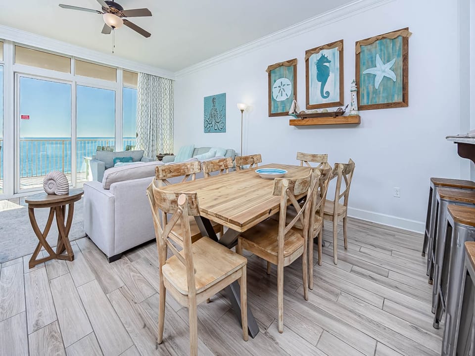 Your beachfront dining space features coastal charm with natural wood furnishings and stunning ocean views through floor-to-ceiling windows.