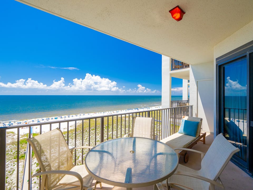 Balcony with a glass table and chairs offers a serene view of the beach and gulf, perfect for relaxing moments