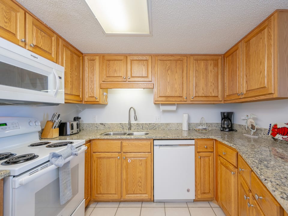 The fully-equipped kitchen features warm wood cabinetry, a breakfast bar with white stools, and granite countertops