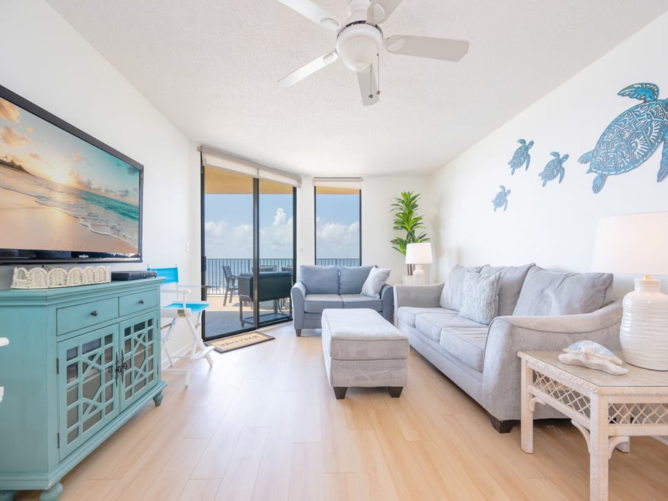 Bright living area featuring a comfortable gray sofa with queen sleeper, dining table with chairs, and a stunning beach view