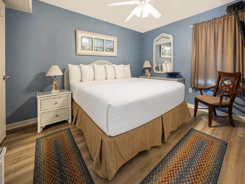 Cozy bedroom featuring a king bed with decorative pillows, a wicker nightstand, and a charming mirror against a blue wall
