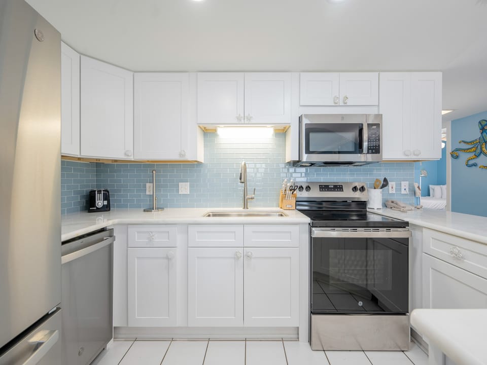 Bright white cabinetry complements the blue backsplash in this modern kitchen, featuring a sleek countertop and ample storage