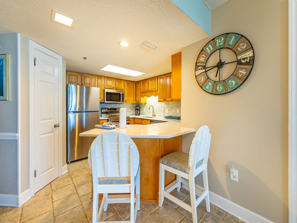 Bright wood cabinetry complements the kitchen, featuring a breakfast bar with white stools and a stylish wall clock