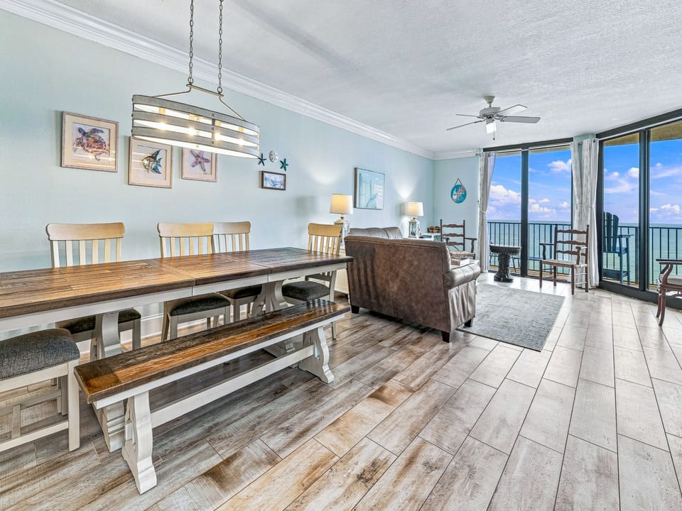 Dining area features a rustic table with a decorative vase, surrounded by light-colored chairs and accented by coastal decor