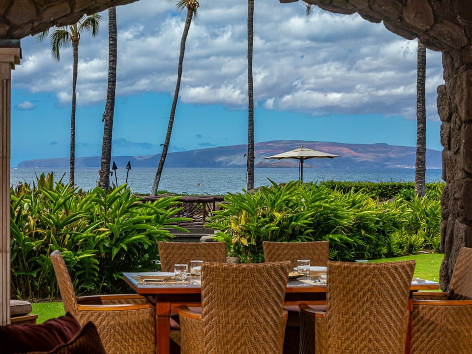 Dine alfresco with sweeping views of turquoise waters and distant mountains framed by swaying palms and lush tropical gardens—your perfect island escape awaits.