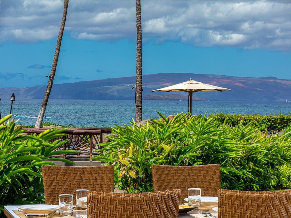 Outdoor dining with breathtaking ocean and mountain views. Your table awaits, surrounded by tropical palms and lush greenery, with the gentle sea breeze as your companion.