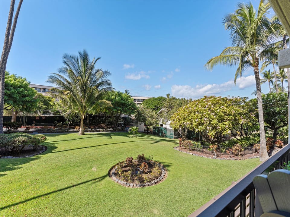 Lush tropical gardens with swaying palms and manicured lawns create a serene island escape, visible from the private balcony and surrounding the property.
