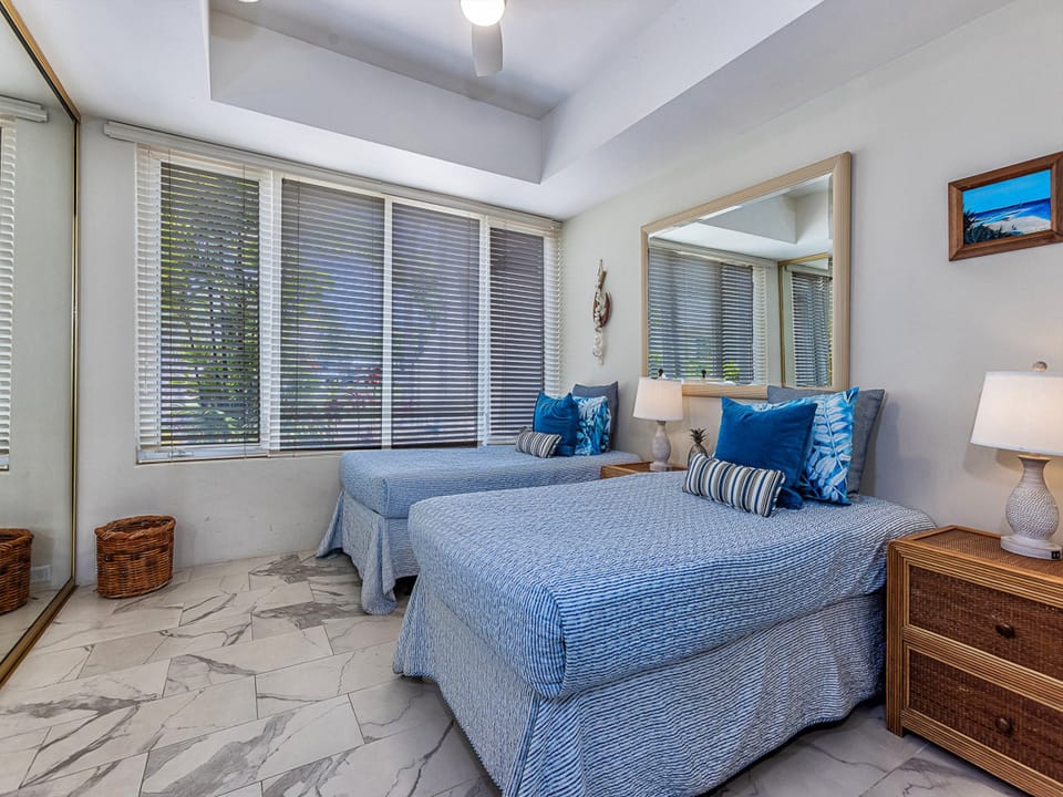 Relax in your airy bedroom with twin beds dressed in coastal blue linens, natural wicker furnishings, and soft light filtering through the windows—your restful sanctuary awaits.