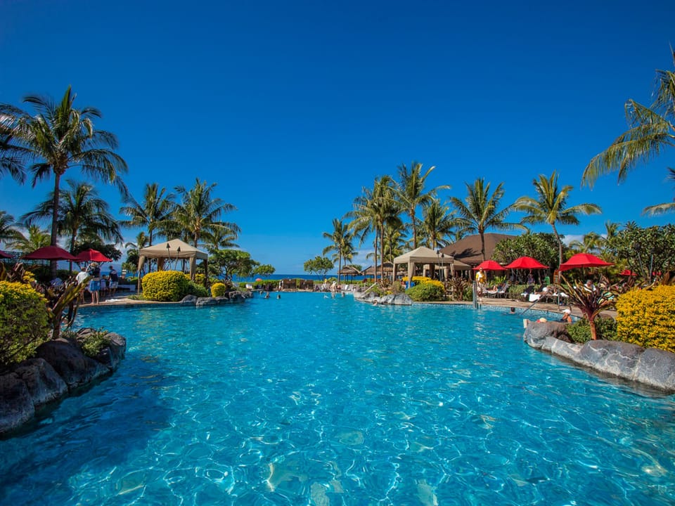 A sprawling lagoon-style pool surrounded by tropical palms and landscaped gardens, with cabanas and lounge chairs inviting relaxation under brilliant skies.