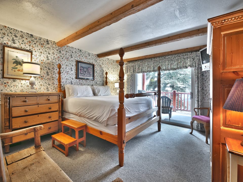 Main bedroom features a 4 post wooden king-sized bed with white linen, flowered wall paper and wooden night stands