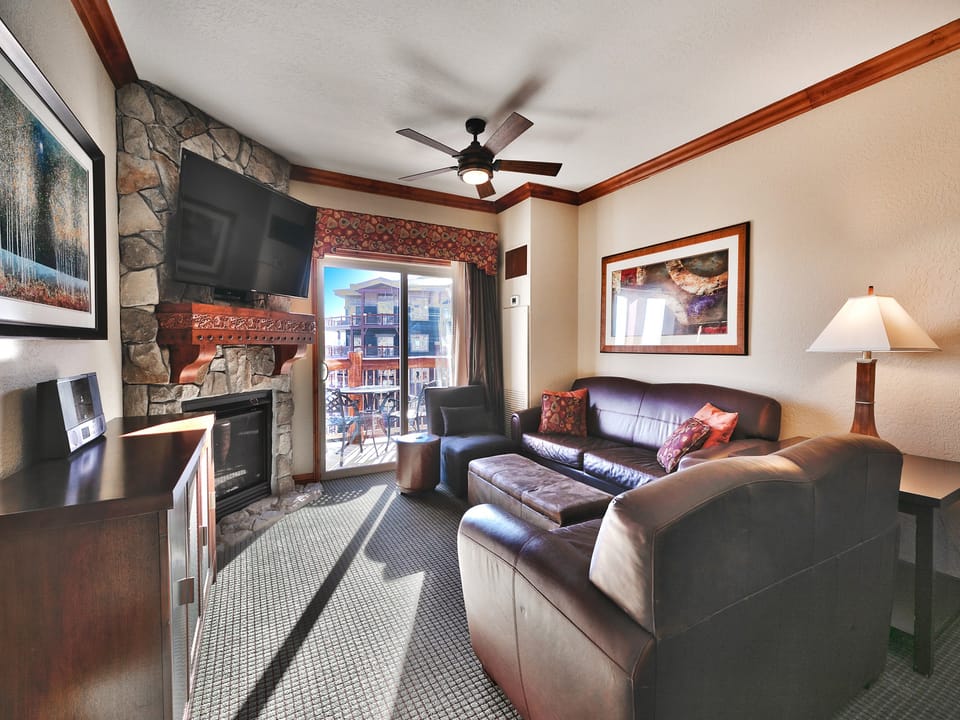 Living room with warm tones, bright natural light, gas fireplace and large screen TV, queen sofa sleeper