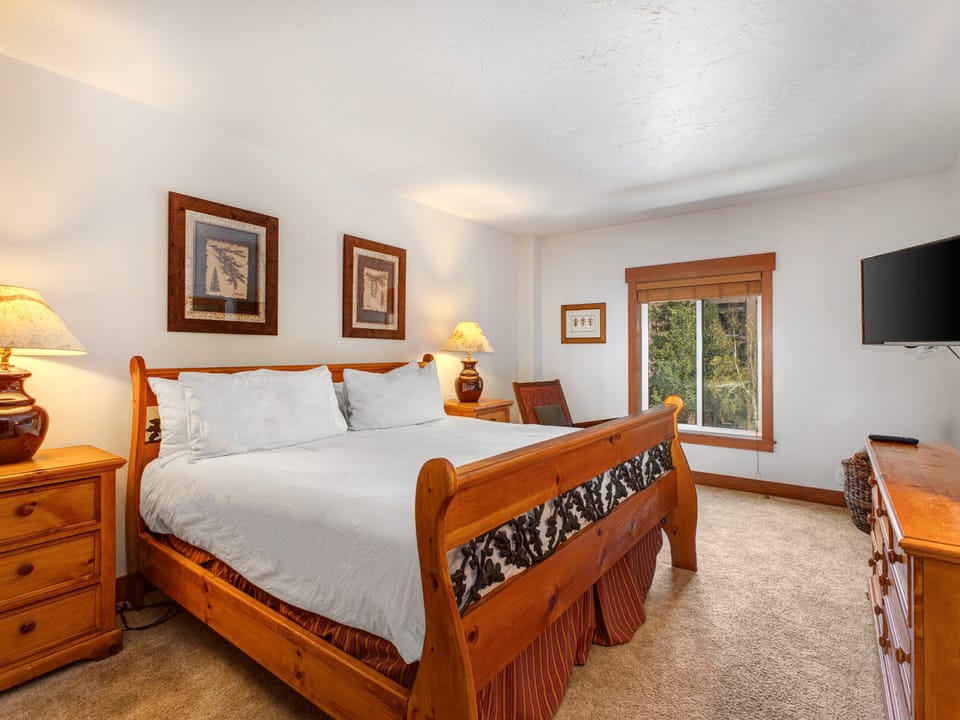 Park Station 134's main suite with a king size bed, white linens and pillows, and a window with trees outside.