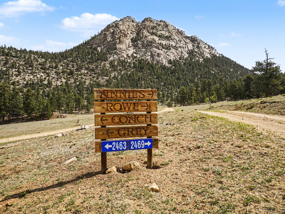 Wooden road sign marks the scenic mountain area, with rugged peaks and forested slopes creating a dramatic natural backdrop for outdoor adventures.