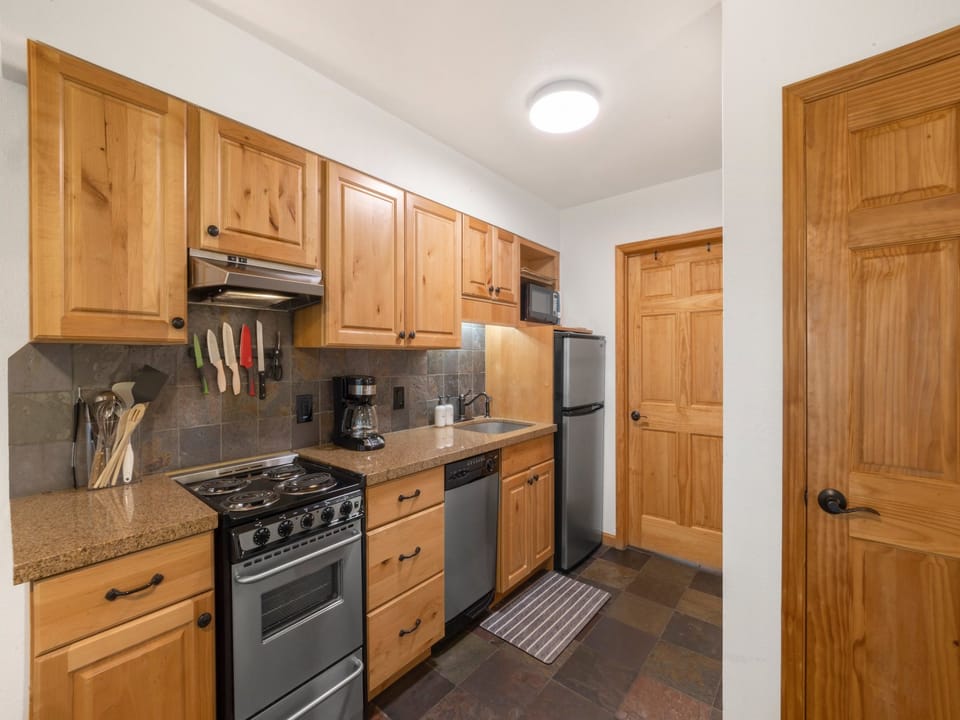A compact kitchen fully equipped with everything you need—including a full fridge, oven, range, microwave, and dishwasher—for easy meal prep.