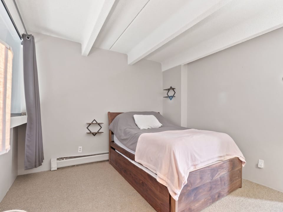 Slip into peaceful rest in your cozy bedroom, where clean white beams frame the ceiling and soft neutral tones invite relaxation.