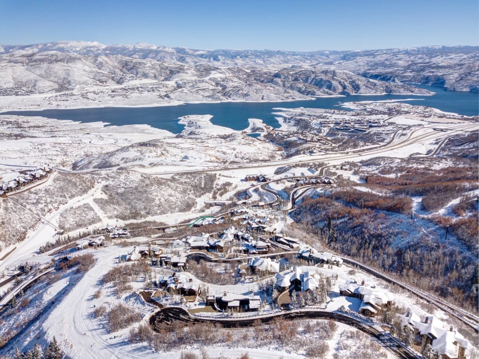 Breathtaking aerial view of a snow-covered mountain village nestled beside pristine lake waters, showcasing the stunning winter landscape surrounding this destination.