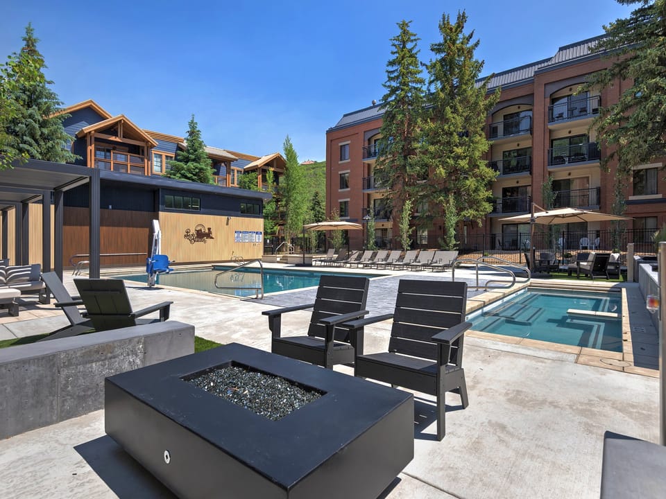 Modern poolside retreat featuring two sparkling pools, a cozy fire pit, and lounge chairs surrounded by alpine trees and mountain architecture.