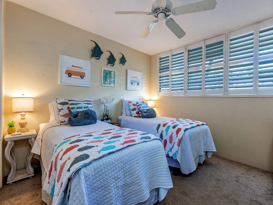 Your coastal-themed bedroom features two plush beds dressed in cheerful fish-patterned linens, perfect for family or friends. Gentle beach breezes flow through plantation shutters while playful touches create a relaxed, seaside feel.