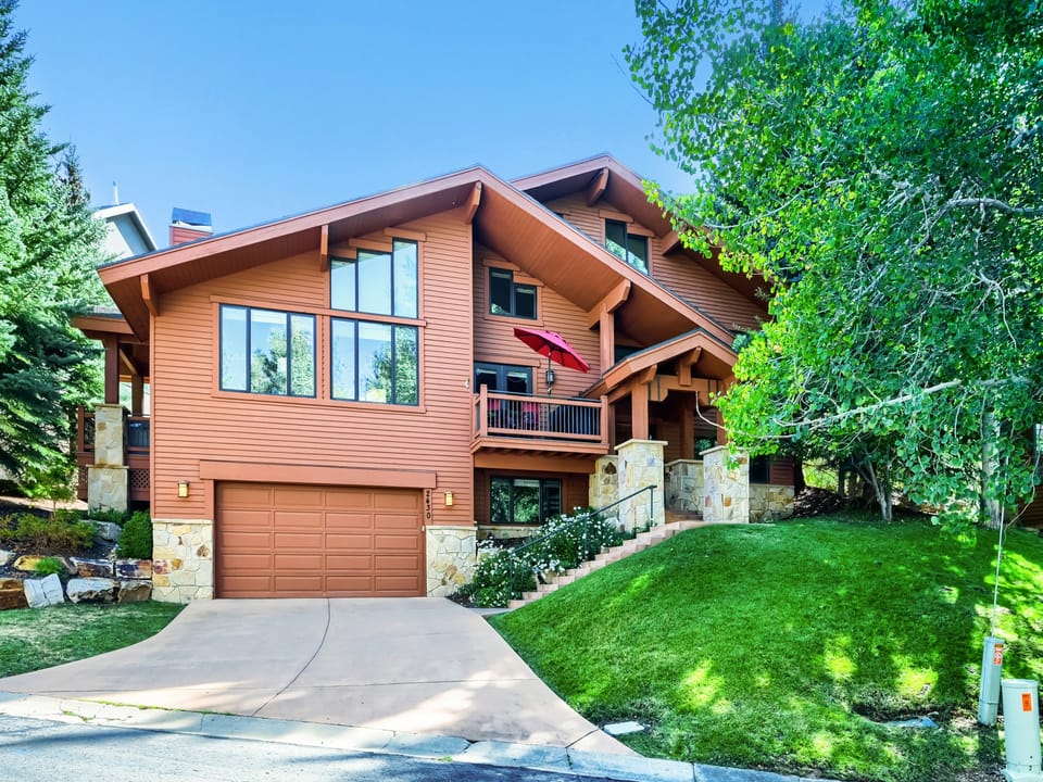 A charming mountain retreat with warm wood siding, expansive windows, and stone accents nestled among tall trees and manicured lawn. Private driveway leads to an inviting multi-level home.