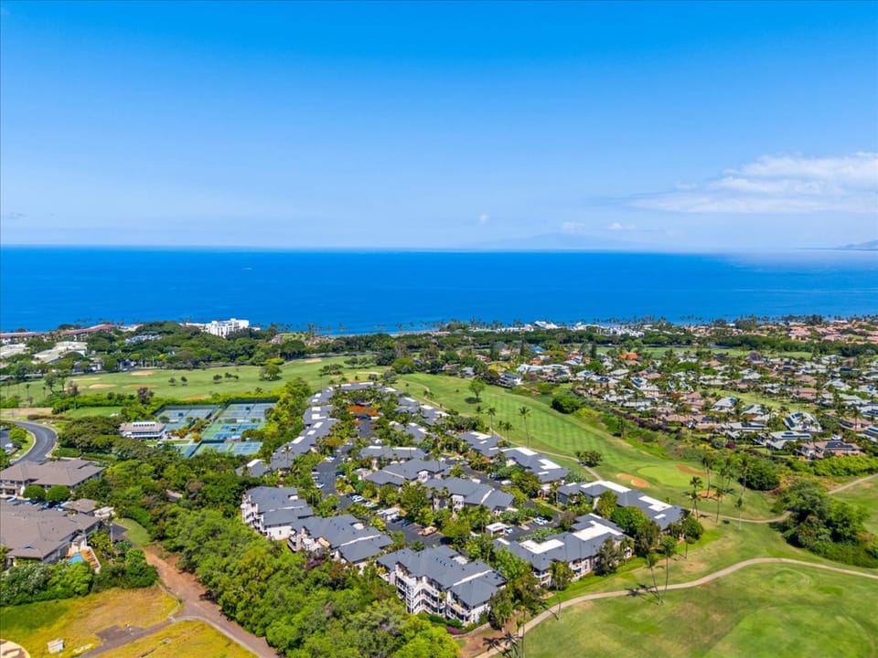 Aerial view of a coastal property nestled between a lush golf course and the sparkling blue Pacific Ocean, offering a serene Hawaiian escape.