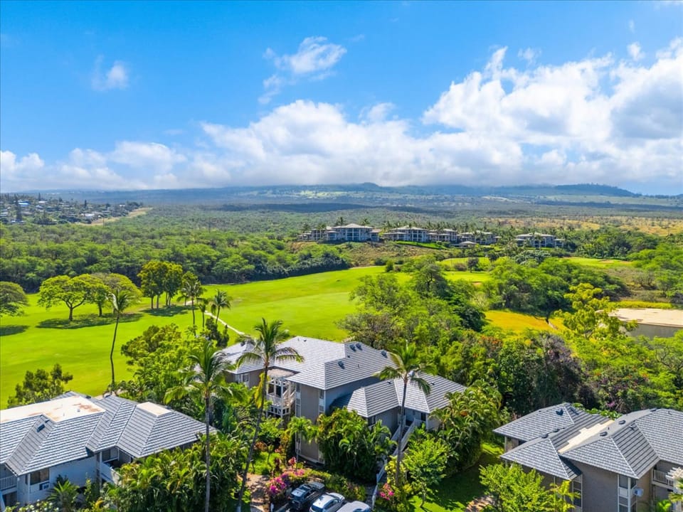 Aerial view showcasing the property nestled among lush tropical greenery with a pristine golf course and distant ocean vistas framing this serene island retreat.