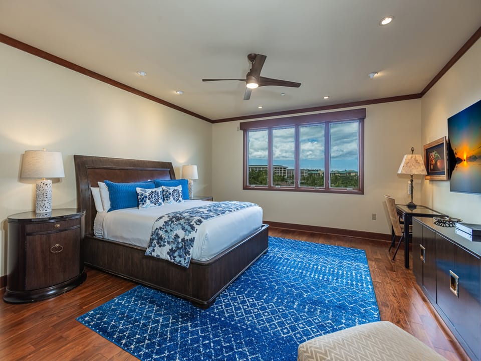 Step into your spacious sanctuary, where rich hardwood floors and a ceiling fan create a breezy retreat. Your king-size bed is dressed in coastal blues, inviting you to unwind beneath the soft glow of elegant bedside lamps.