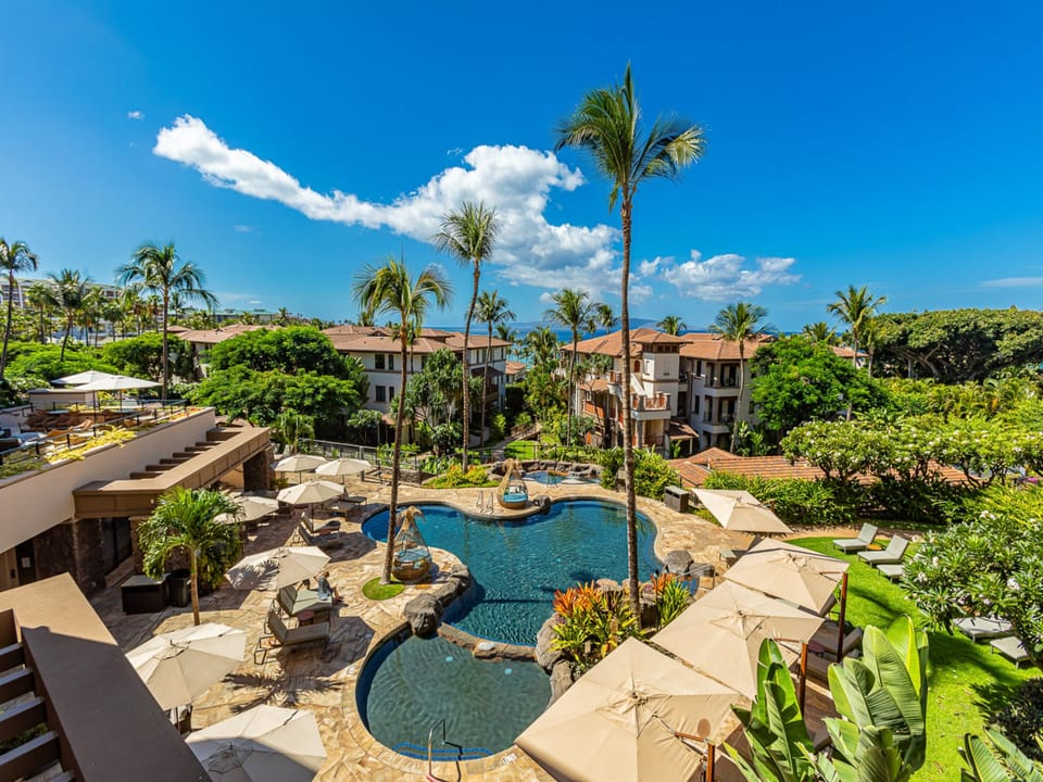 Resort grounds featuring tropical landscaping, sparkling pools with natural stone accents, and comfortable lounging areas surrounded by swaying palms and lush greenery.