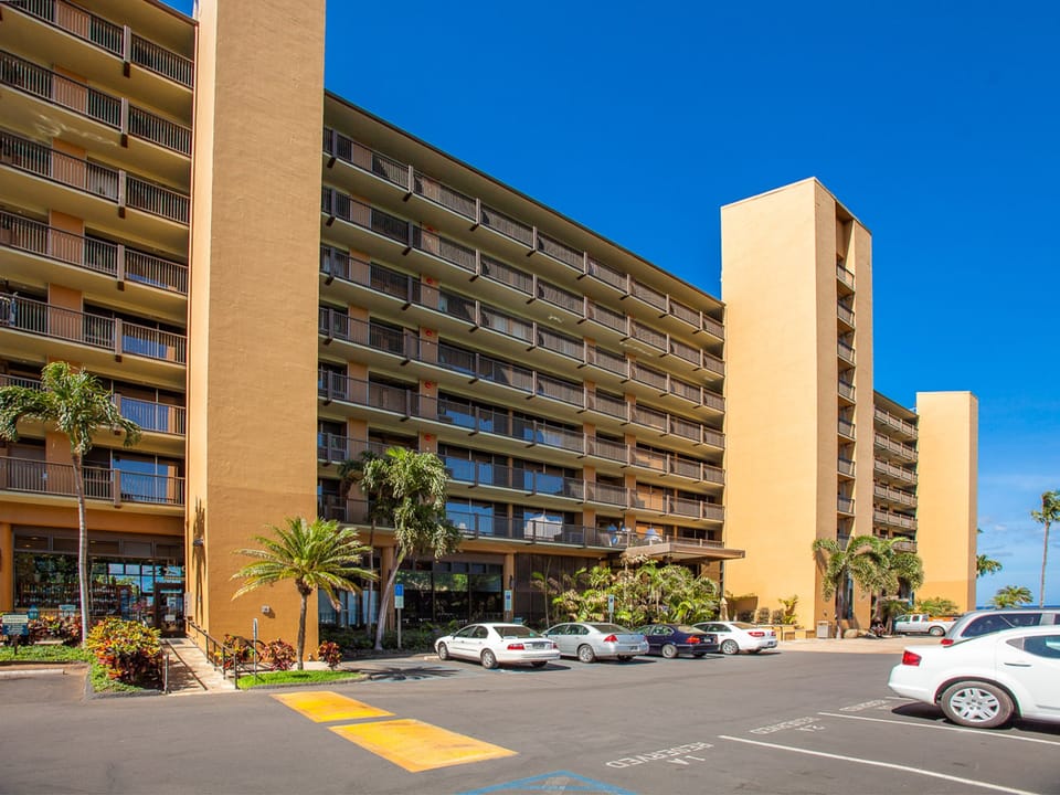 Modern hotel complex with convenient parking and tropical landscaping under clear blue skies.