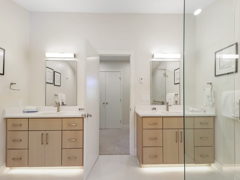 Your spacious dual-vanity bathroom offers sleek modern design with warm wood cabinetry and abundant counter space. Bright ambient lighting and a frameless glass shower create a spa-like retreat for your morning and evening routines.