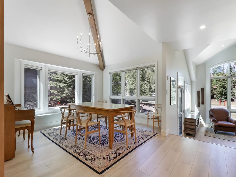 Gather around the handcrafted dining table beneath soaring vaulted ceilings and rustic wooden beams. Sunlight pours through expansive windows, framing peaceful treetop views while you share meals in this warm, airy space.