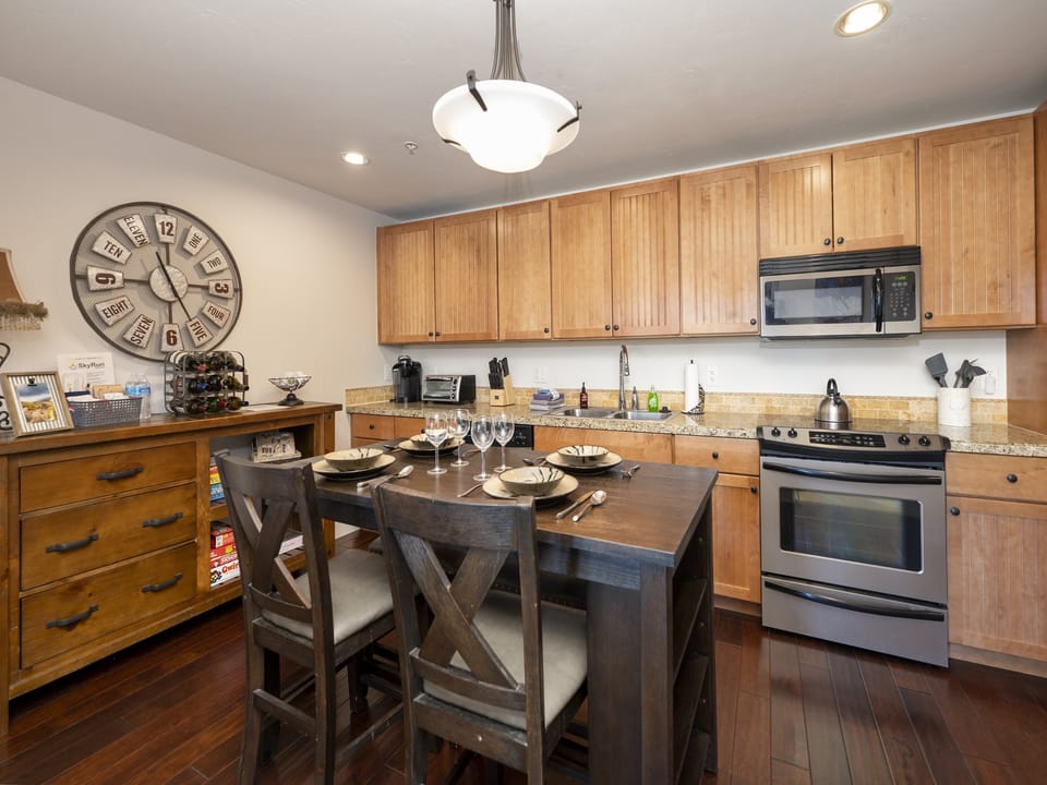 A modern kitchen with wooden cabinets, stainless steel appliances, a dark wooden dining table set for four