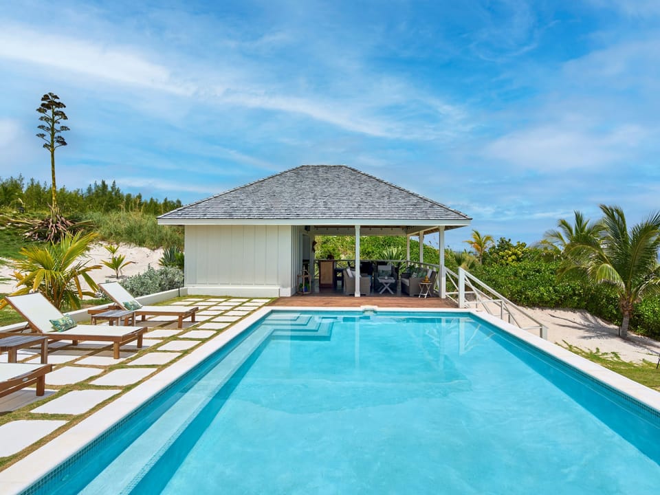The Pool House, an open-air, covered space for guests to gather.  It features a lounge area, a six-seat dining table, and a fully stocked bar on the honor system.