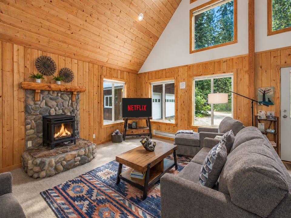 Cozy up in your inviting living room featuring a crackling fireplace, vaulted wood ceilings, and comfortable seating—perfect for your evening entertainment and relaxation.