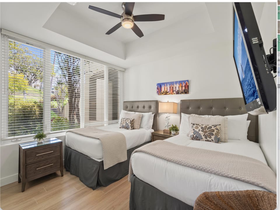 Settle into comfort in this bright bedroom with two plush beds, perfect for sharing your getaway. A ceiling fan keeps you cool, and those big windows let in warm natural light and garden views.