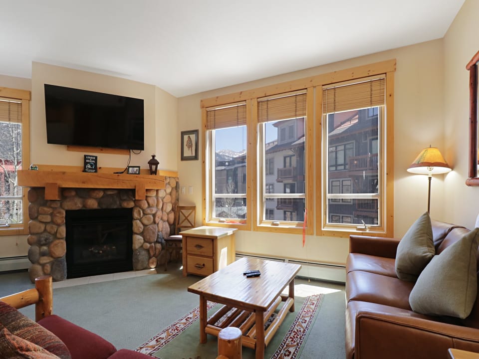 Cozy up in your mountain retreat with a stone fireplace, leather sofa, and stunning alpine views through large windows.