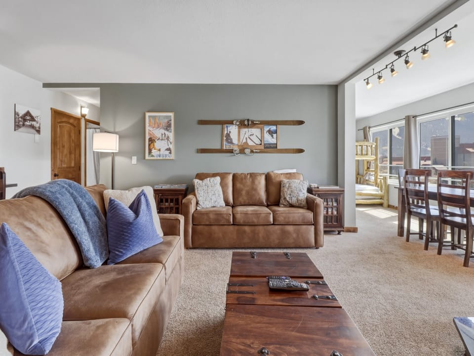 Unwind in your spacious living room featuring plush leather sofas with cozy blue accents and rustic mountain-inspired décor.