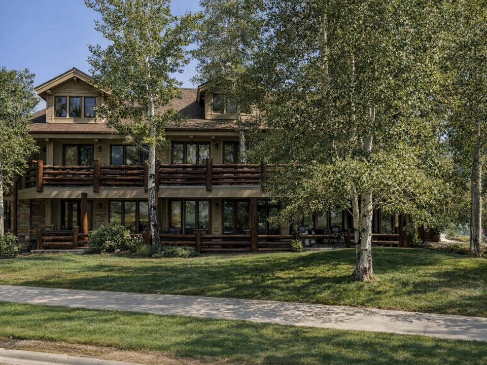 Stunning mountain lodge-style property featuring rustic wood accents and multiple balconies, surrounded by mature aspen trees in a peaceful residential setting.