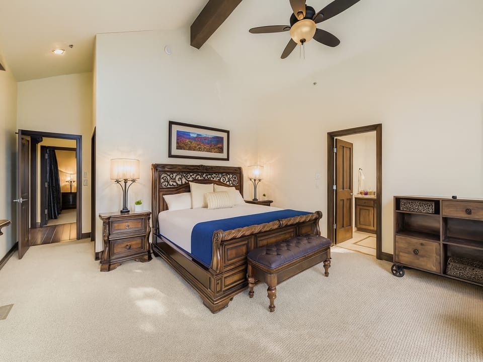 Relax in your elegant master bedroom featuring rich wood furnishings, soft lighting, and a cozy ceiling fan to keep you comfortable throughout your stay.
