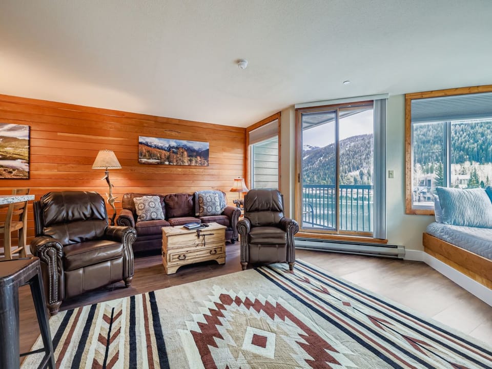 Relax in your cozy living room with stunning mountain views, featuring comfortable leather seating and warm wood accents that create the perfect alpine retreat atmosphere.