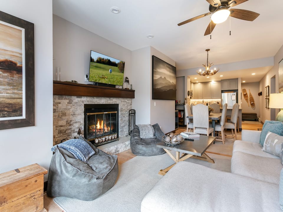 A cozy living room with a fireplace, TV, bean bags, sofa, and large artwork on the walls. The room extends to an adjoining dining area and modern kitchen with stainless steel appliances.